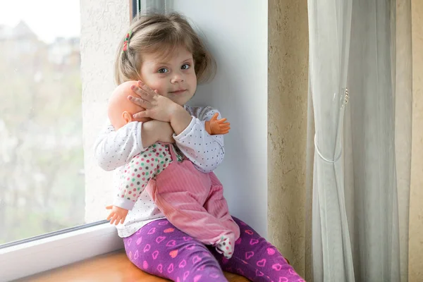 Niña sentada en el alféizar de la ventana con un juguete en las manos — Foto de Stock