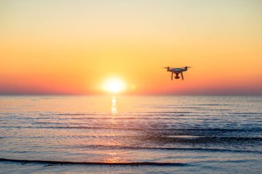 Deniz günbatımının arka planında uçan dron