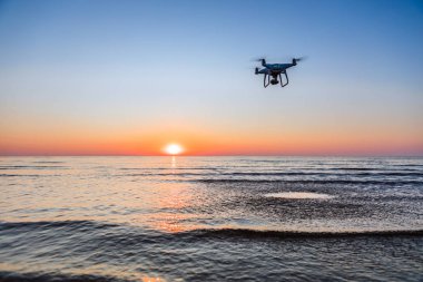 Deniz günbatımının arka planında uçan dron