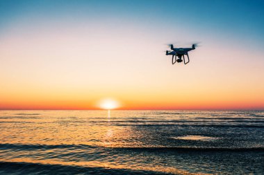 Deniz günbatımının arka planında uçan dron