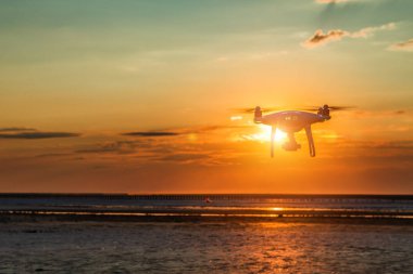 Deniz günbatımının arka planında uçan dron
