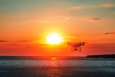 Deniz günbatımının arka planında uçan dron