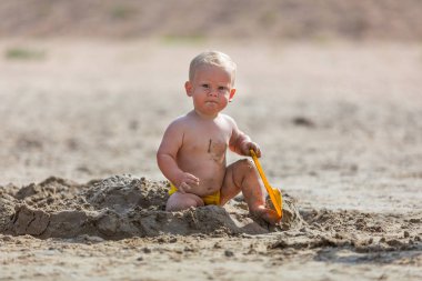 Küçük çocuk deniz kenarında kumla oynuyor.