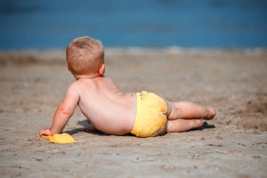 Küçük çocuk deniz kenarında kumla oynuyor.