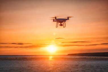 Deniz günbatımının arka planında uçan dron