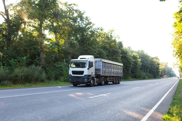 Gün batımında kırsal bir arazide beyaz bir kamyon geliyor.