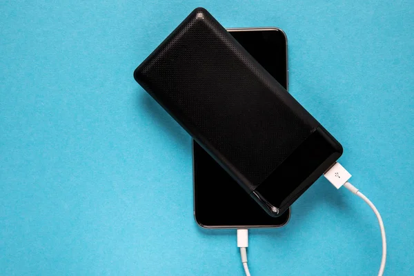 Black Power bank charges smartphone isolated on blue background — ストック写真