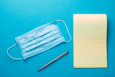 Coronavirus. Renkli bir arkaplanda defter kopyalama alanı, tıbbi maske, kalem ve tabletler.