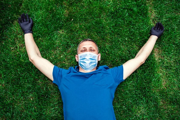 young man in face medical mask lies on green grass. Resting after self-isolation, quarantine.