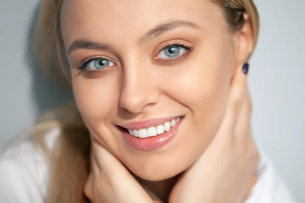 Porträt einer lächelnden Blondine in einer weißen Bluse auf hellem Hintergrund. — Stockfoto