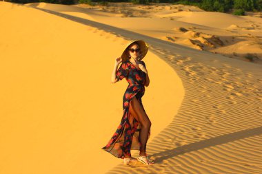 Asyalı kadın yürüyor ve kum tepeciğinin tadını çıkarıyor. Gün batımında bir kızın silueti.