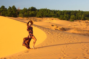 Asyalı kadın yürüyor ve kum tepeciğinin tadını çıkarıyor. Gün batımında bir kızın silueti.
