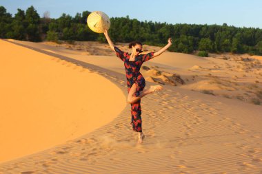 Asyalı kadın yürüyor ve kum tepeciğinin tadını çıkarıyor. Gün batımında bir kızın silueti.