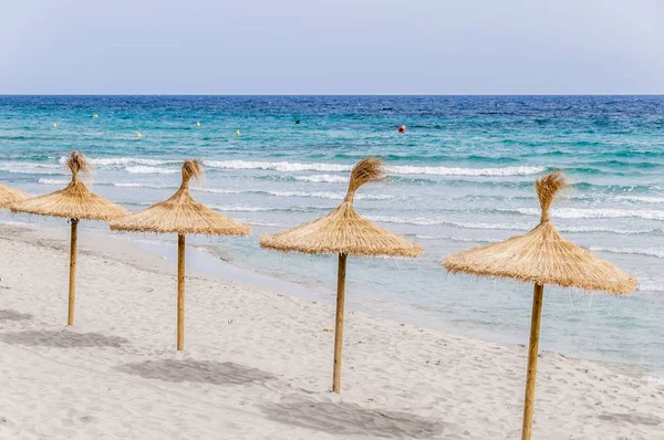 Stro paraplu's op zand strand. — Stockfoto