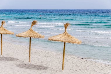 Kum plajı üzerinde hasır şemsiyeler.