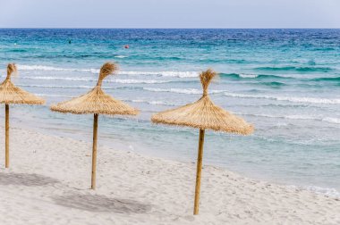 Kum plajı üzerinde hasır şemsiyeler.