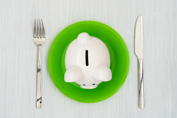 消費者の概念を救う 緑のプレート上のピギーバンクフォークとナイフ — ストック写真