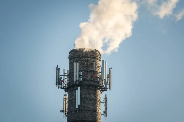 複数の携帯電話のアンテナを持つ高工業用煙突の上 澄んだ青空の背景に出てくる煙 — ストック写真