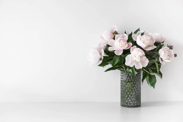 Ramo de tiernas peonías rosadas en jarrón cerca de la pared blanca —  Fotos de Stock