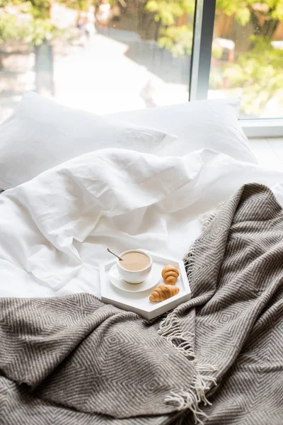 Micul dejun confortabil în pat, ceașcă de cafea și croissante pe alb și — Fotografie, imagine de stoc