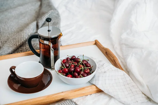 Fresh healthy vegan breakfast in bed, green tea and cherry in morning bedroom interior close-up