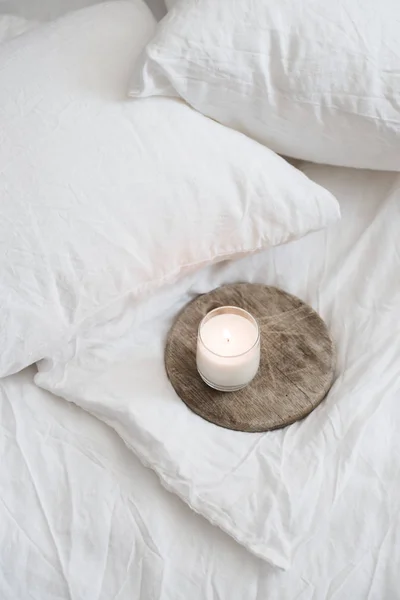 Burning candle on wooden tray on white natural linen — Stock Photo, Image