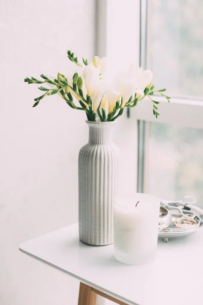 Ramillete de freesias blancas en jarrón y vela aromática sobre mesa —  Fotos de Stock