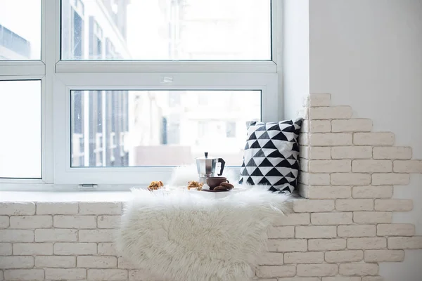Cozy winter home arrangement on windowsill, coffee and cookies on tray with pillow and faux fur white blanket
