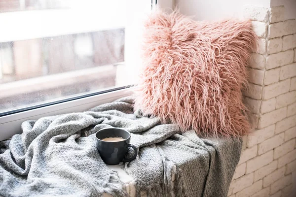 Tazza di caffè, coperta a maglia e soffice cuscino sul davanzale della finestra accogliente — Foto Stock