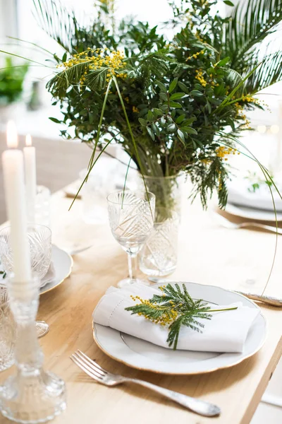 Beautiful springtime table setting with green leaves and mimosa branches, bright white table dinner decoration — Stock Photo, Image