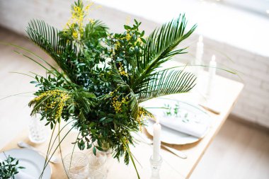 Güzel bahar sofra yeşil yaprakları ve mimoza dalları, parlak beyaz masa akşam yemeği dekorasyonu ile