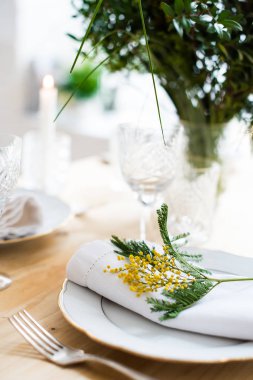 Güzel bahar sofra yeşil yaprakları ve mimoza dalları, parlak beyaz masa akşam yemeği dekorasyonu ile