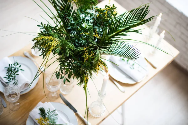 Bella tavola primaverile con foglie verdi e rami di mimosa, luminoso tavolo bianco decorazione cena — Foto Stock