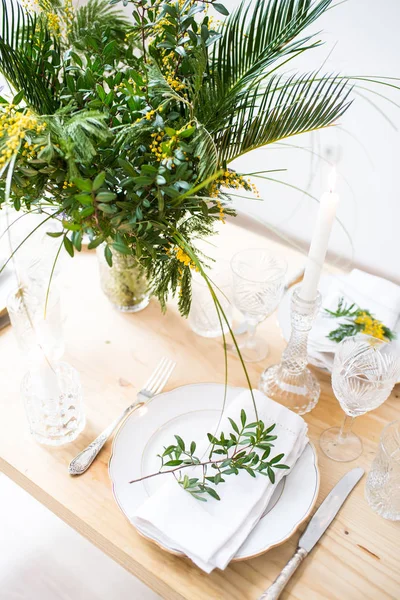 Beautiful springtime table setting with green leaves and mimosa branches, bright white table dinner decoration — Stock Photo, Image