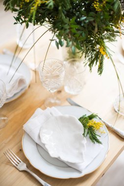 Güzel bahar sofra yeşil yaprakları ve mimoza dalları, parlak beyaz masa akşam yemeği dekorasyonu ile