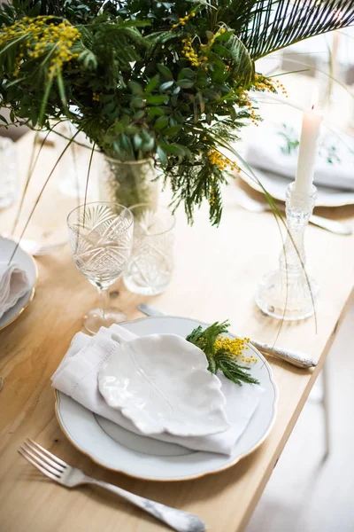 Schöne frühlingshafte Tischdekoration mit grünen Blättern und Mimosenzweigen, strahlend weiße Tischdekoration — Stockfoto