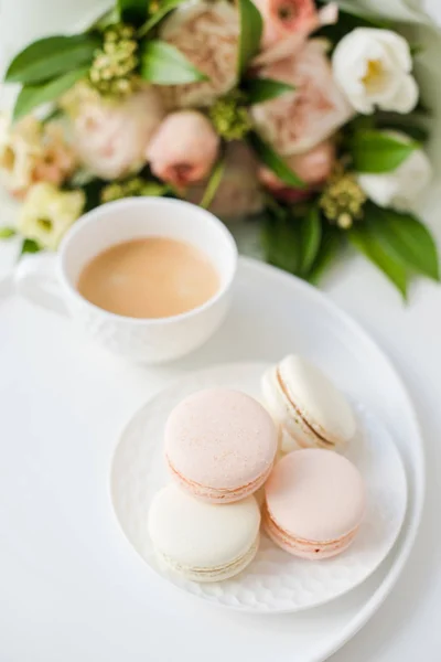 Κομψό γλυκό επιδόρπιο μακαρόνια, φλιτζάνι καφέ και παστέλ χρώματα μπεζ λουλούδια ανθοδέσμη — Φωτογραφία Αρχείου