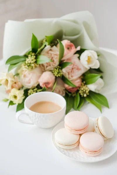 Macarons de sobremesa doce elegante, xícara de café e pastel colorido buquê de flores bege — Fotografia de Stock