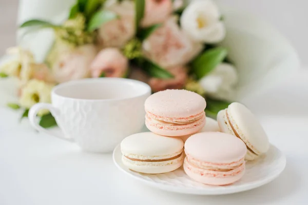 Elegant sweet dessert macarons, cup of coffee and pastel colored beige flowers bouquet — Stock Photo, Image