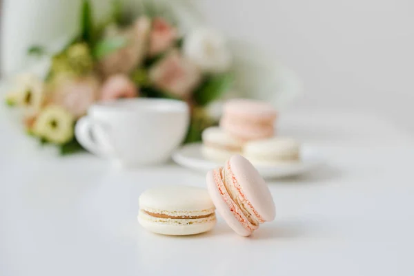 Elegant sweet dessert macarons, cup of coffee and pastel colored beige flowers bouquet — Stock Photo, Image