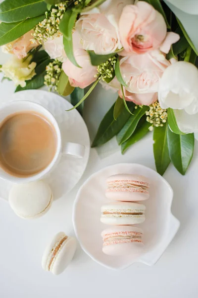 Elegant sweet dessert macarons, cup of coffee and pastel colored beige flowers bouquet — Stock Photo, Image