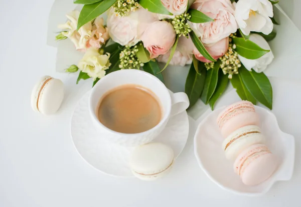 Elegant sweet dessert macarons, cup of coffee and pastel colored beige flowers bouquet — Stock Photo, Image