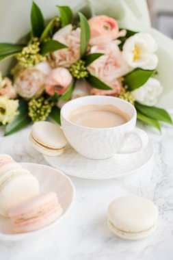 Beyaz mermer üzerinde zarif tatlı tatlı macarons, kahve ve pastel renkli bej çiçekler Buket fincan