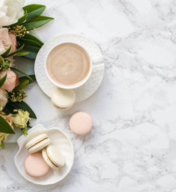 Beyaz mermer üzerinde zarif tatlı tatlı macarons, kahve ve pastel renkli bej çiçekler Buket fincan