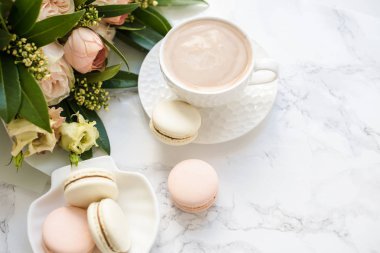 Beyaz mermer üzerinde zarif tatlı tatlı macarons, kahve ve pastel renkli bej çiçekler Buket fincan