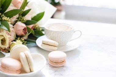 Beyaz mermer üzerinde zarif tatlı tatlı macarons, kahve ve pastel renkli bej çiçekler Buket fincan