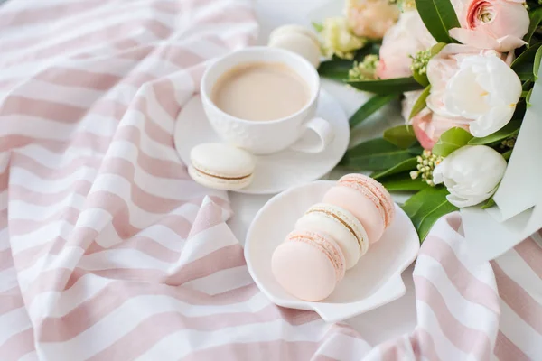 Elegant sweet dessert macarons, cup of coffee and pastel colored beige flowers bouquet — Stock Photo, Image