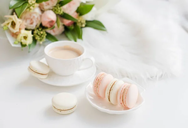 Elegante zoete dessert Macarons, kopje koffie en pastelkleurige beige bloemen boeket — Stockfoto