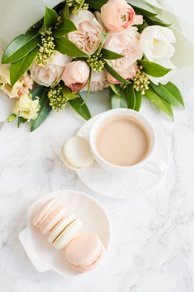 Elegancki słodki makarony deser, filiżanka kawy i pastelowy kolor beżowy kwiaty bukiet na białym marmurze — Zdjęcie stockowe