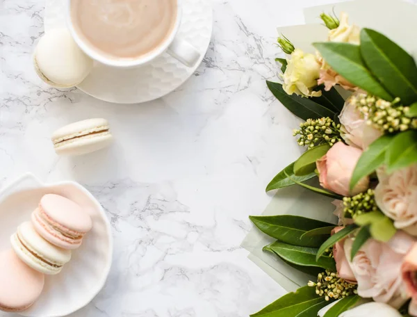 Κομψό γλυκό επιδόρπιο μακαρόνια, φλιτζάνι καφέ και παστέλ χρώματα μπεζ λουλούδια μπουκέτο σε λευκό μάρμαρο — Φωτογραφία Αρχείου